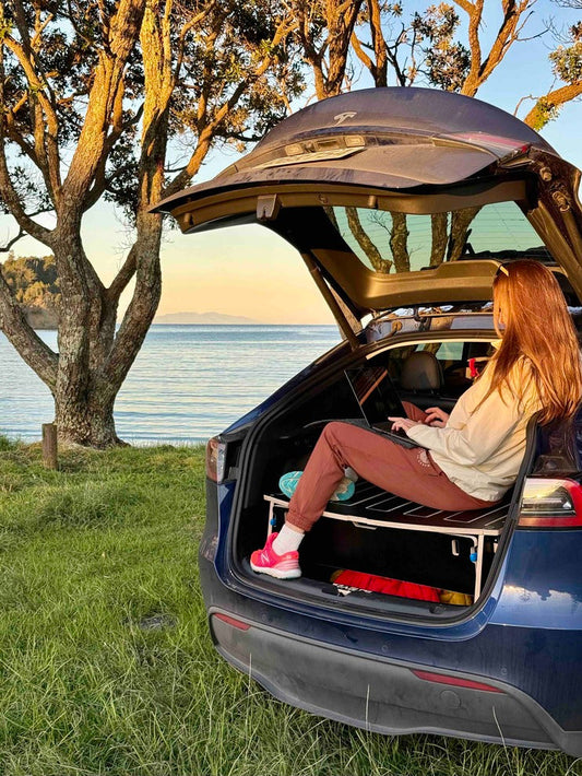 Working inside Tesla on Teraglide camping platform parked near the ocean during car camping trip