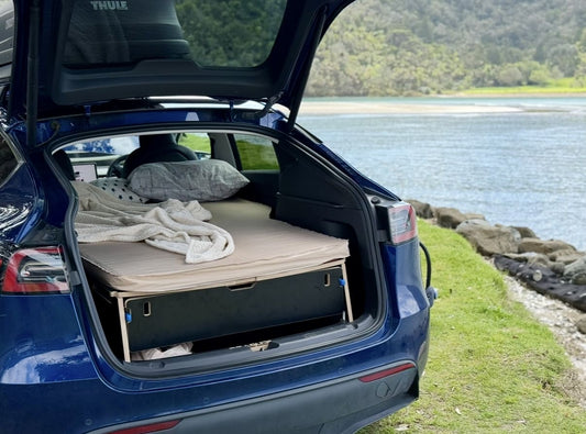 nterior of Tesla Model Y showing Teraglide Pro platform bed, fridge storage in sub-trunk, and camping setup at night