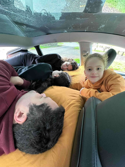 Family car camping setup with kids preparing breakfast beside a trunk bed platform in a forest campsite