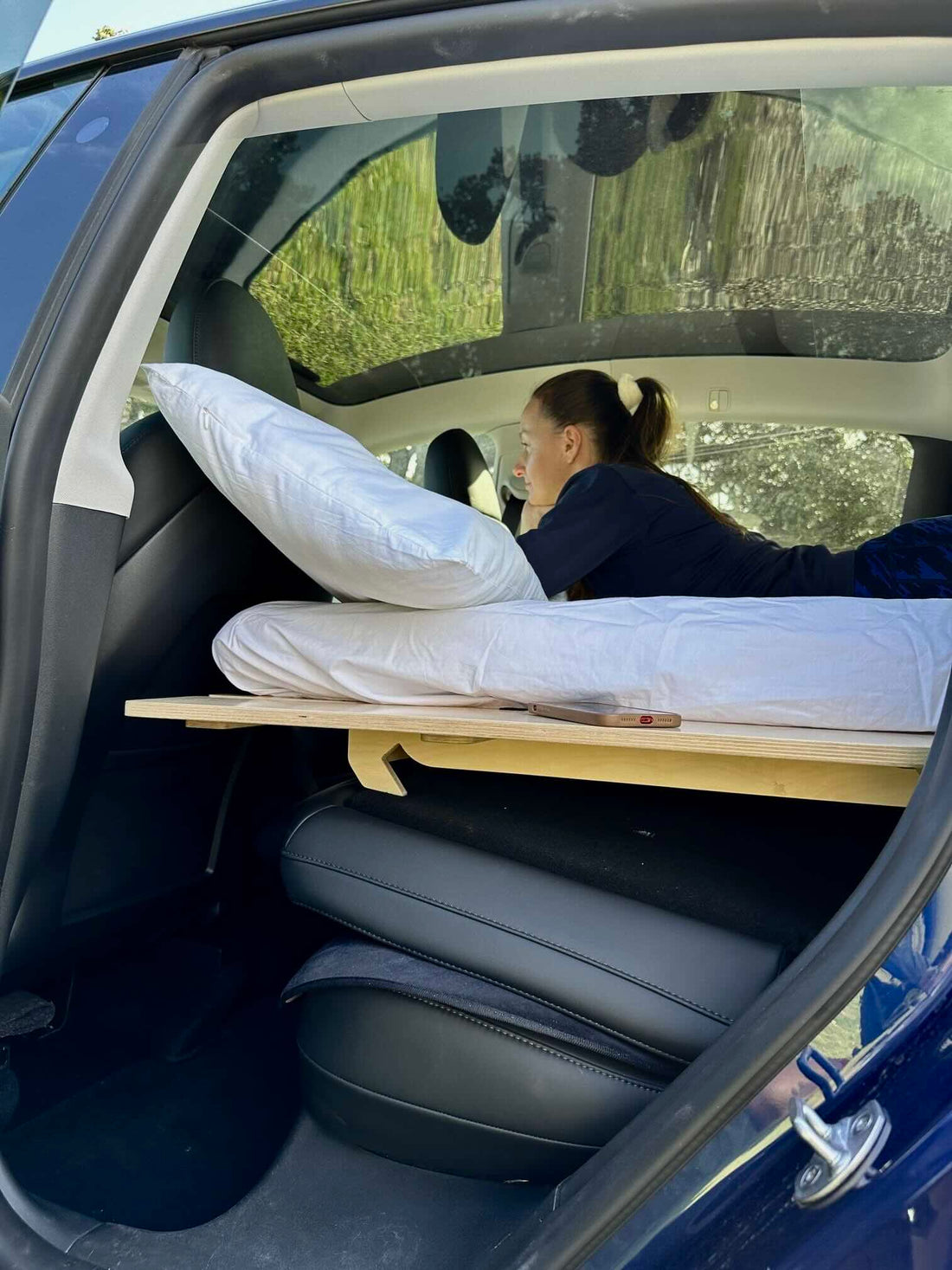 Woman relaxing on a Teraglide platform bed inside a Tesla Model Y, showing how the car transforms into a cozy sleeping space
