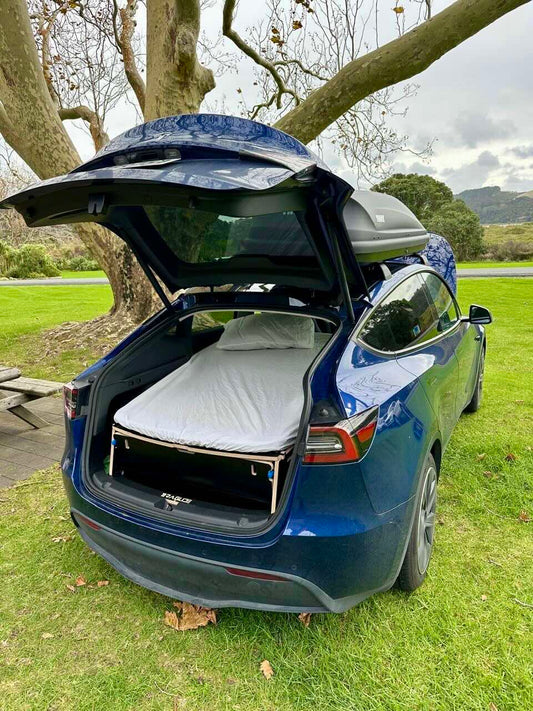 Tesla Model Y parked in a grassy Australian campsite with the Teraglide PRO camping conversion kit set up in the trunk for sleeping