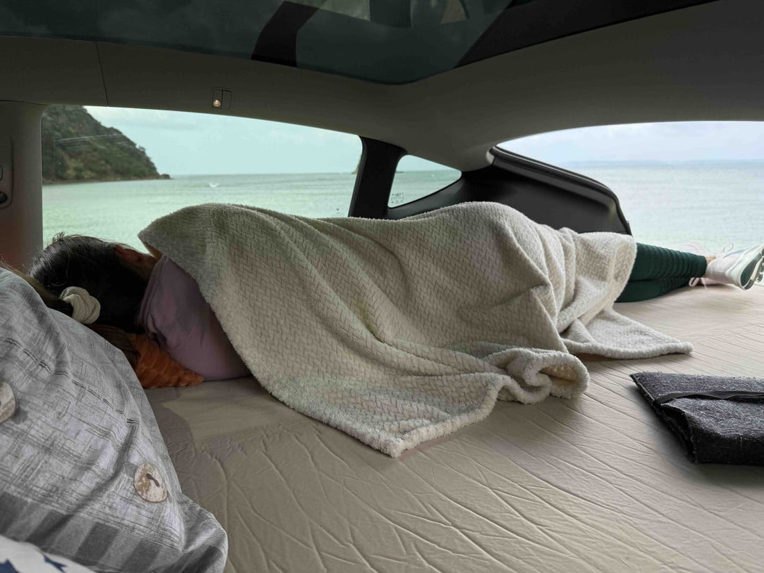 Teraglide Pro car camping platform set up as a flat bed inside Tesla Y, with raindrops visible on the rear window.