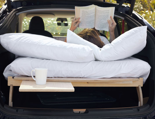 Woman reading a book on a Teraglide camping platform set up in the trunk, enjoying a peaceful moment outdoors in Australia or New Zealand
