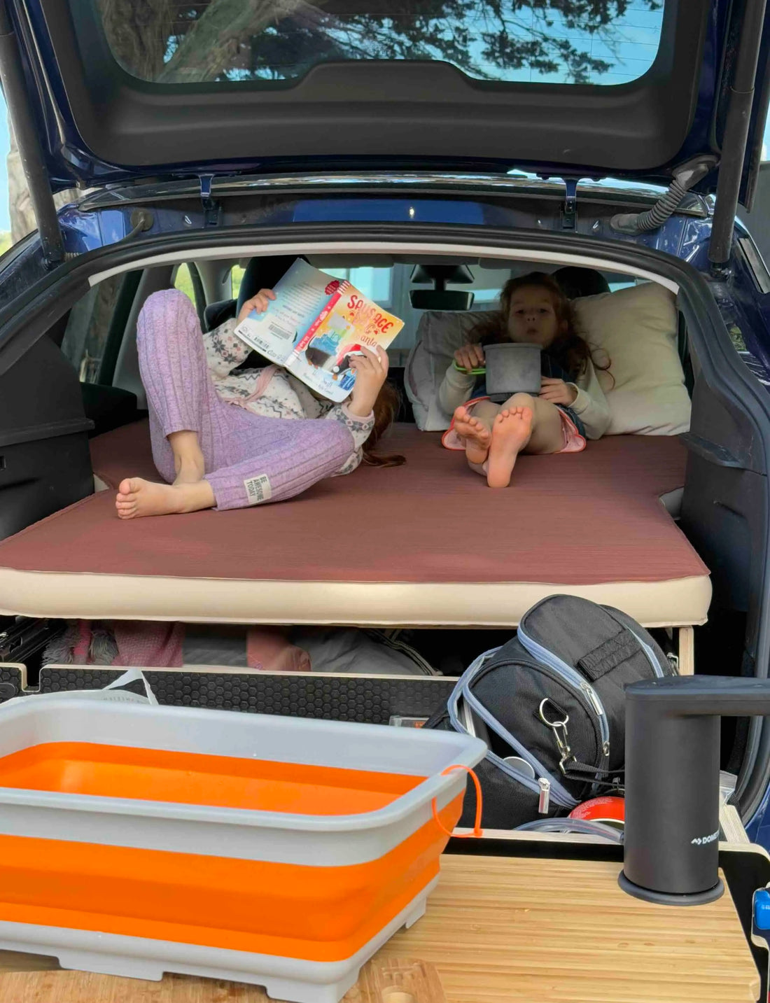 SUV in nature with a Teraglide car camping platform set up as a flat bed in the trunk, showing a quiet, organised in-car sleeping space