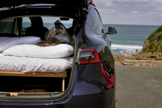 Woman relaxing inside a cozy car camping setup with scenic nature views in the background, showcasing minimalist travel with Teraglide platform
