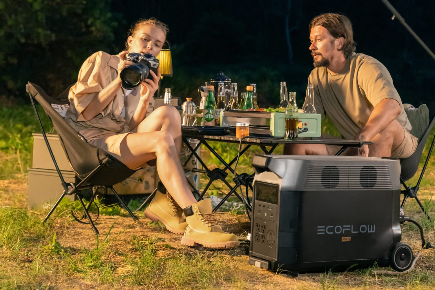 Two people sitting outdoors at night with a camping stove and ecoflow powerbank, surrounded by nature.