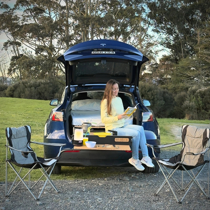 Woman reading a book at the back of a Tesla Model Y with the Teraglide PRO bed behind her